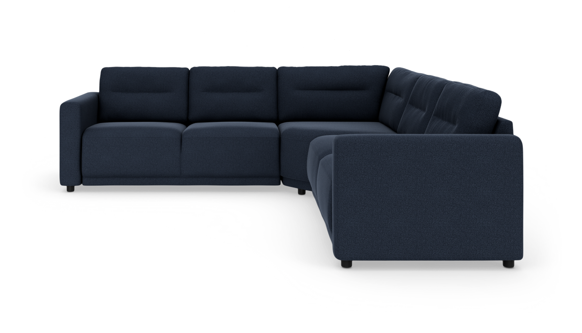 Mørkeblå L‑formet modulsofa i stof set forfra i vinkel på hvid studiobaggrund.