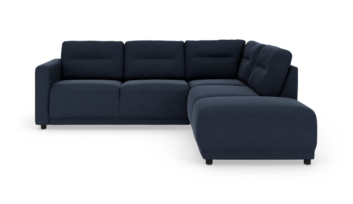 Mørkeblå L‑sofa med chaiselong til højre og polstrede ryghynder på hvid studiobaggrund.