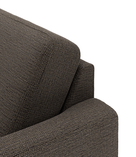 Nærbillede af brungrå stofpolstring på sofa med armlæn og rygpude mod sort baggrund.