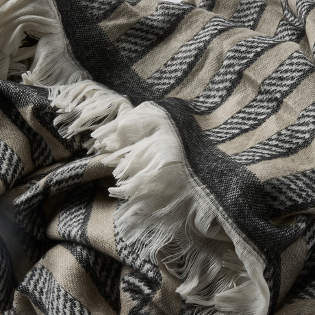 Nærbillede af blød plaid med beige og mørkegråt zigzagmønster og hvide frynser.