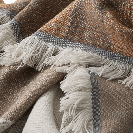 Nærbillede af vævet plaid i beige og rustbrune nuancer med grå kant og hvide frynser.