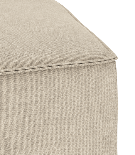 Nærbillede af hjørne på beige stofbetrukket puff/ottoman med synlig piping.