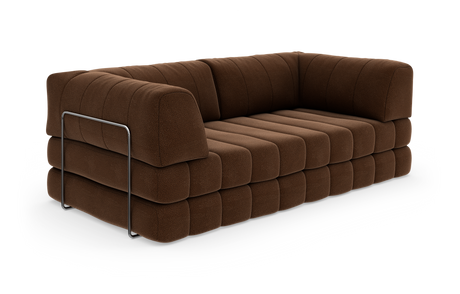 Brun, blød modulsofa med brede, kviltede hynder og en slank metalbøjle som detalje på siden, fritlagt på hvid baggrund.