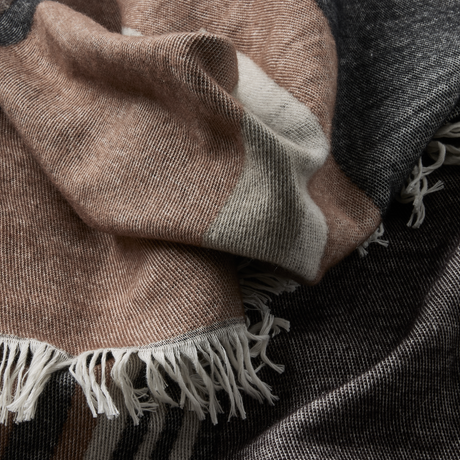 Nærbillede af et blødt plaid med frynser i beige, grå og creme.