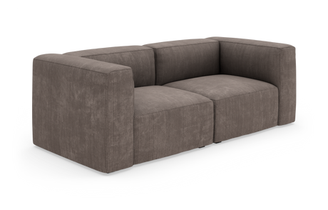 Brungrå modulsofa i bredriflet fløjl (corduroy), tosædet med kraftige armlæn, frilagt på hvid baggrund i trekvart vinkel.