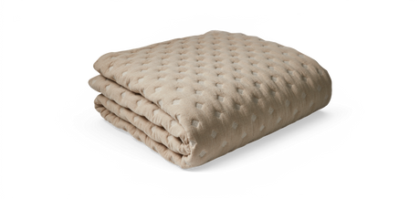 Beige sammenfoldet plaid med quiltet tekstur og diskrete prikker, frilagt på hvid baggrund.
