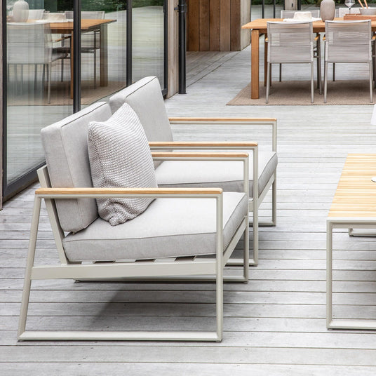 Moderne terrasse med lysegrå loungestole, træ-sofabord og glasfacade med udsigt til grønne træer.