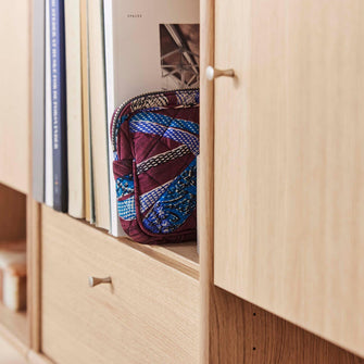 Nærbillede af en reol i lyst træ med bøger, herunder ”Spaces”, og en farverig quiltet toilettaske.