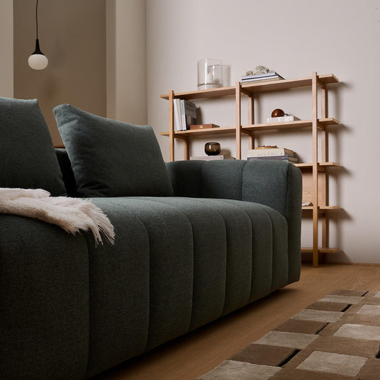 Mørkegrøn sofa i close-up med plaid, træreol med bøger og dekorationer i en skandinavisk stue.