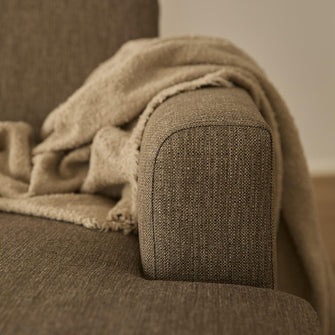 Nærbillede af sofaens armlæn i beige tekstil med et blødt beige tæppe lagt over.