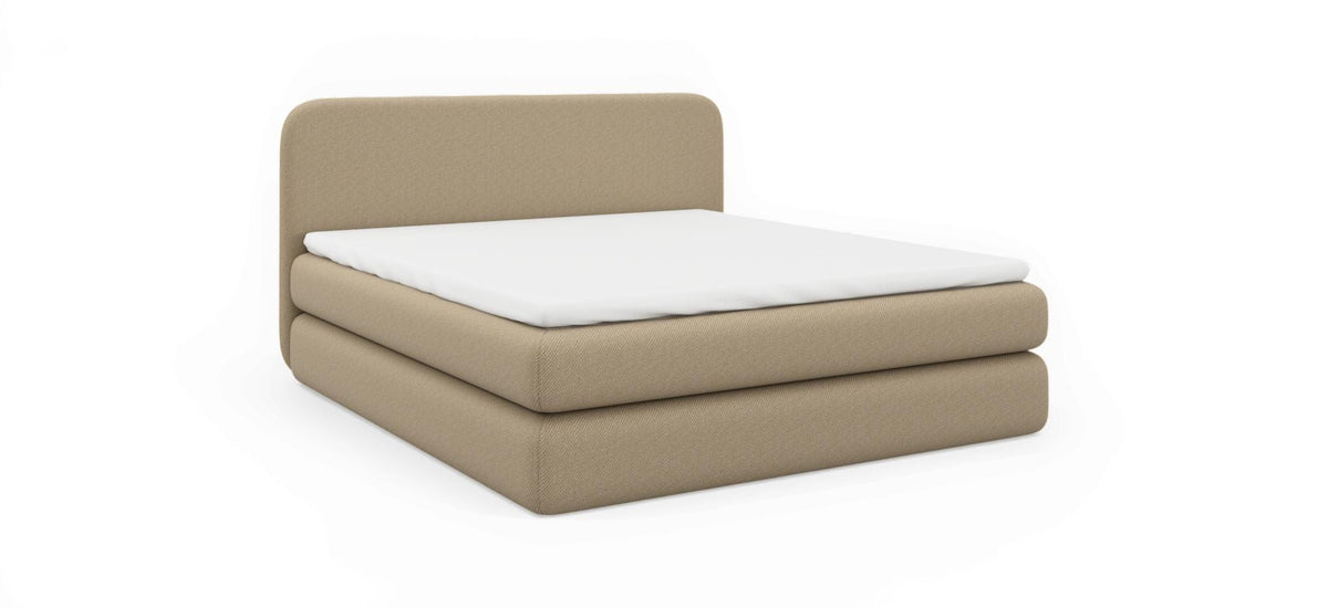 Beige polstret seng med hvid madras, produktbillede på sort baggrund i skrå frontvinkel.