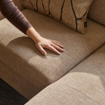 Hånd der trykker på beige stofsofa; IKEA-mærke på puden ses i varmt sollys.