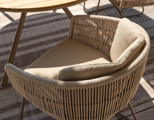 Beige udestol med flettet ryglæn i reb og blød pude, ved rundt bord på terrasse i sollys.