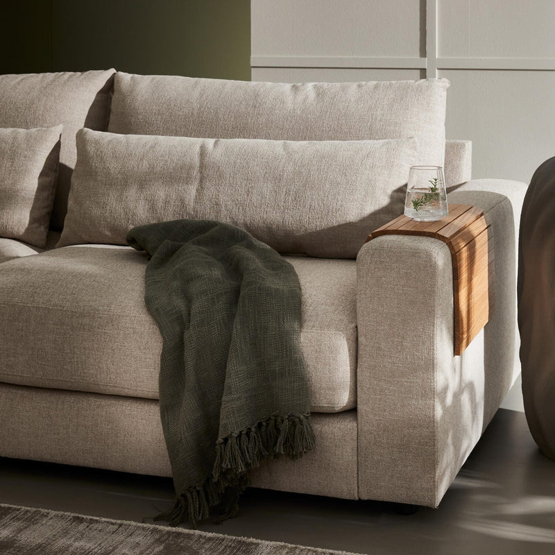 Beige stofsofa med mørkegrønt plaid og træarmbakke med et glas vand i blødt dagslys i stuen.