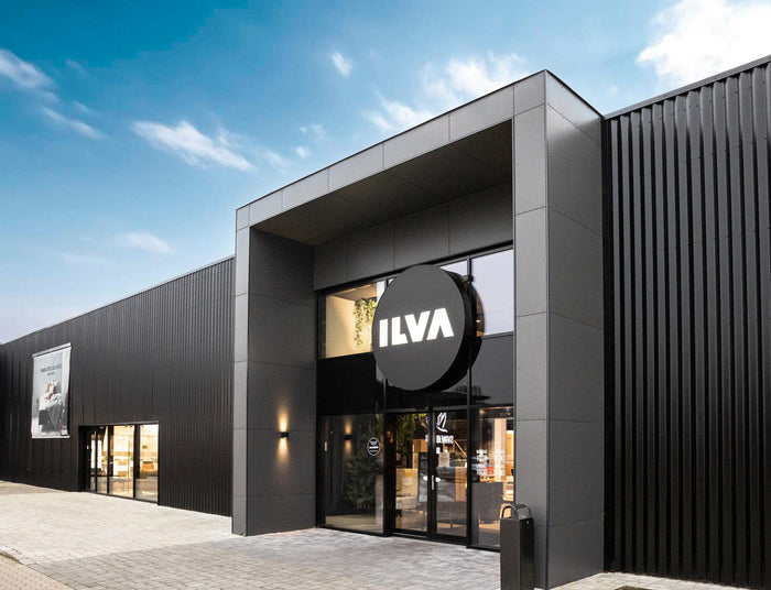Moderne sort butikfacade med stor rund ILVA‑skilt over glasindgangen på en lys dag.