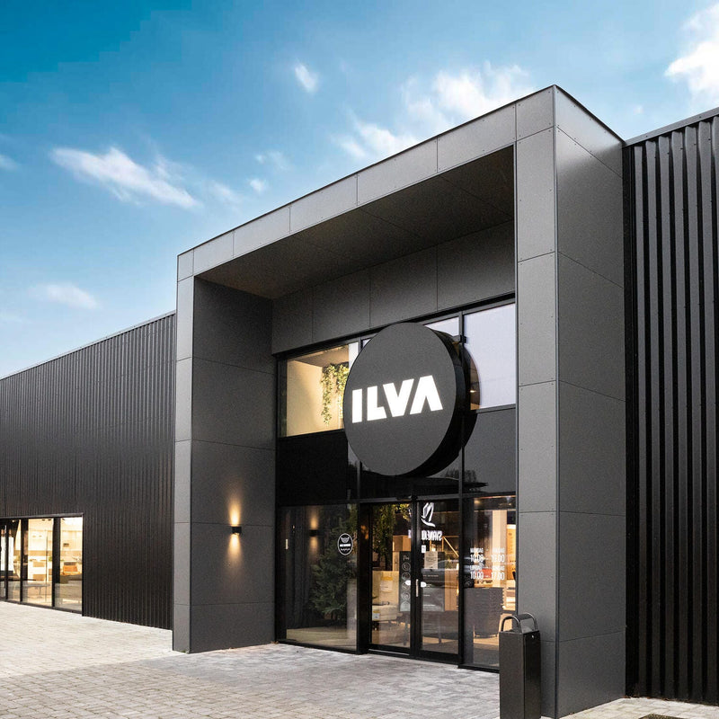 Moderne sort butikfacade med stor rund ILVA‑skilt over glasindgangen på en lys dag.
