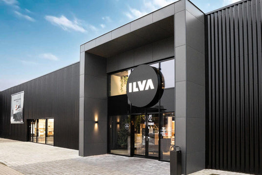 Moderne sort butikfacade med stor rund ILVA‑skilt over glasindgangen på en lys dag.