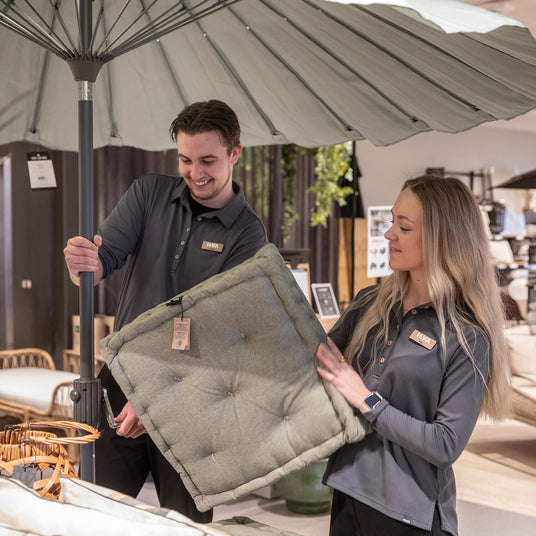 ILVA-butiksmedarbejdere viser en grøn, tufted stolehynde under en stor parasol i butik.