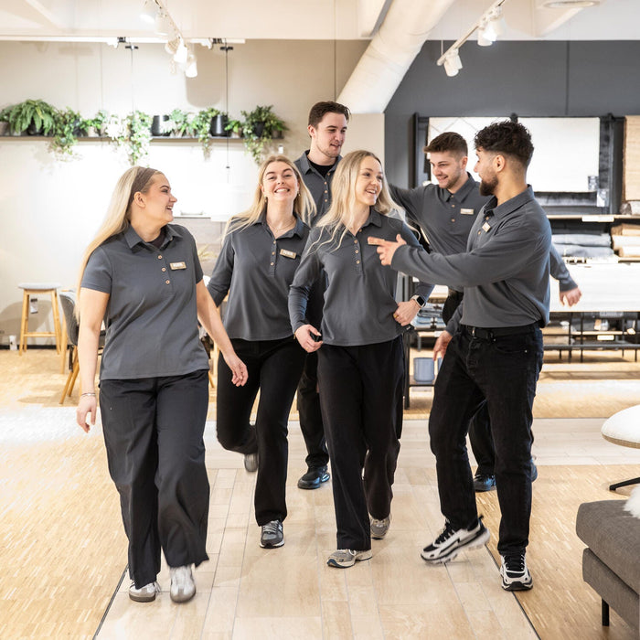 Gruppe butikmedarbejdere i mørkegrå uniform går sammen gennem et møbelshowroom.