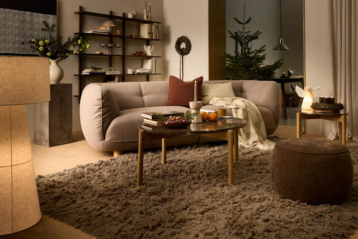 Varm, hyggelig stue med beige sofa, langluvet tæppe, sofabord med lys og appelsiner, krans og juletræ i baggrunden.