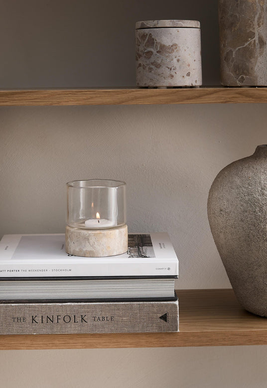Hylde med glaslyslygte på stenfod oven på bøgerne ”The Weekender – Stockholm” og ”The Kinfolk Table”, ved siden af en stenvase.