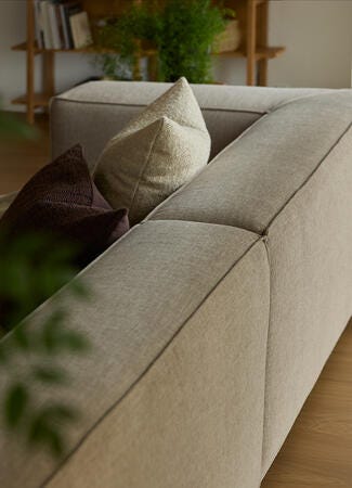 Beige stofsofa med neutrale puder i en lys stue med trægulv og grønne planter.