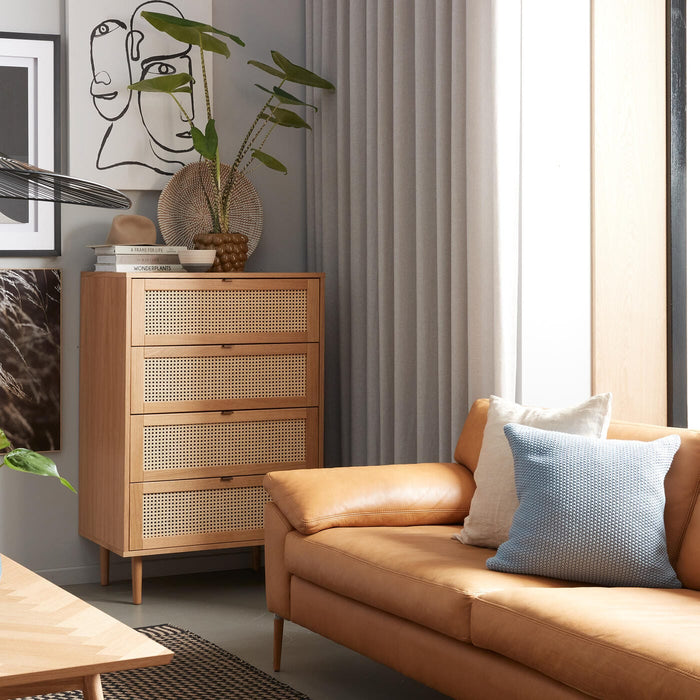 Lyst stue i skandinavisk stil med karamelfarvet lædersofa, skab med rattanfronter, grafisk vægkunst, sort pendel og grønne planter; ovenpå ligger bøger, bl.a. ”WONDERPLANTS”.