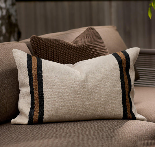 Aflang beige pude med sorte og brune striber i begge ender på en brun udendørs sofa.