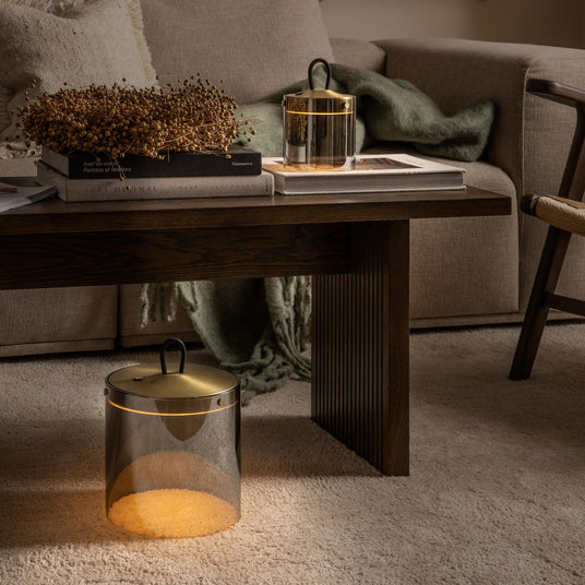 Hyggelig stue med mørkt sofabord på tæppe, beige sofa med grøn plaid og varme portable lamper på bord og gulv; tørrede kviste ligger på bøgerne Soft Minimal og Axel Vervoordt: Portraits of Interiors (Flammarion).