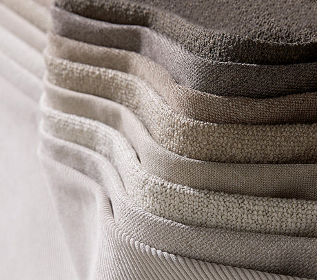 Stak af stofprøver i neutrale beige- og grå nuancer med varierede teksturer.