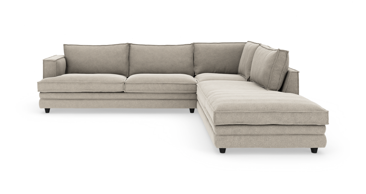 Beige L‑formet hjørnesofa med chaiselong til højre og løse ryghynder.