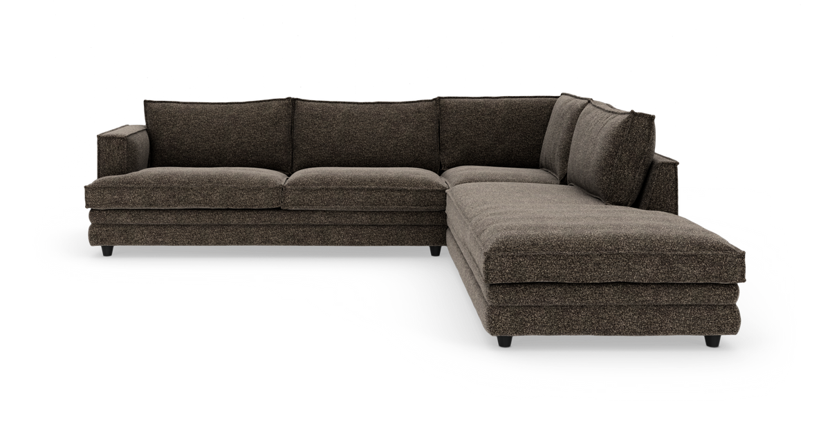 Mørkebrun L‑sofa med højrevendt chaiselong, polstret stof, bløde rygpuder og lave sorte ben, frilagt på hvid baggrund.