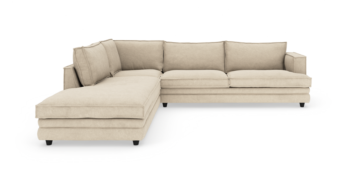 Beige L-sofa med chaiselong, bløde sæde- og ryghynder på sorte ben, frilagt mod hvid baggrund.
