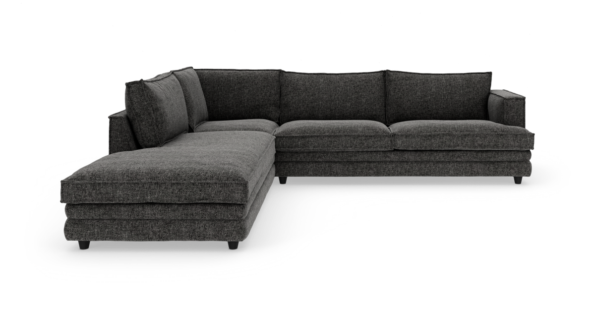 Mørkegrå L‑sofa med venstrevendt chaiselong, bløde rygpuder og slanke ben, fritstående på hvid baggrund.