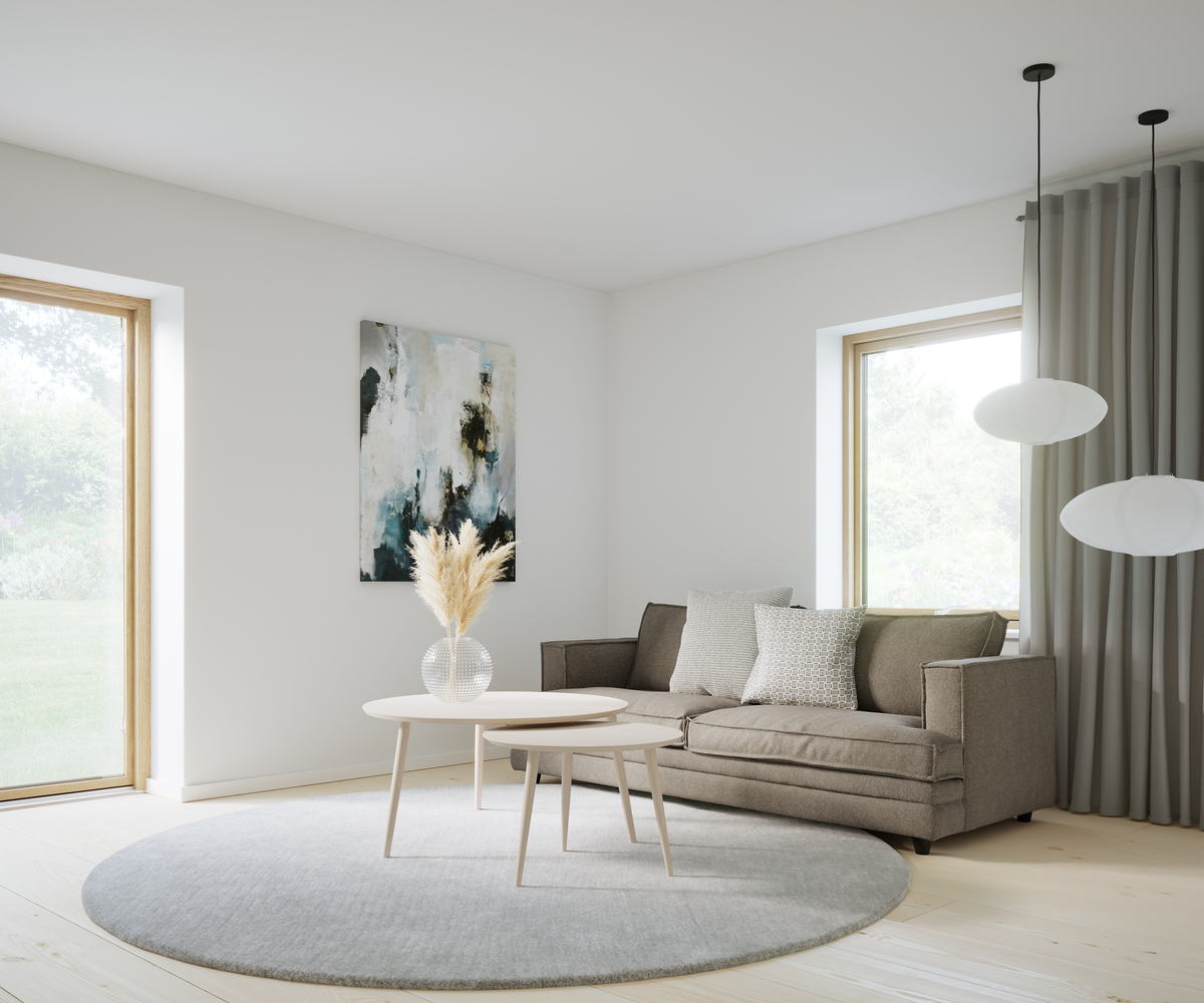 Lyst stue med beigegrå sofa, to runde lyse sofaborde og en glasvase med pampasgræs på et rundt gråt tæppe; abstrakt vægbillede, grå gardiner og to hvide pendler ved store vinduer med dagslys.