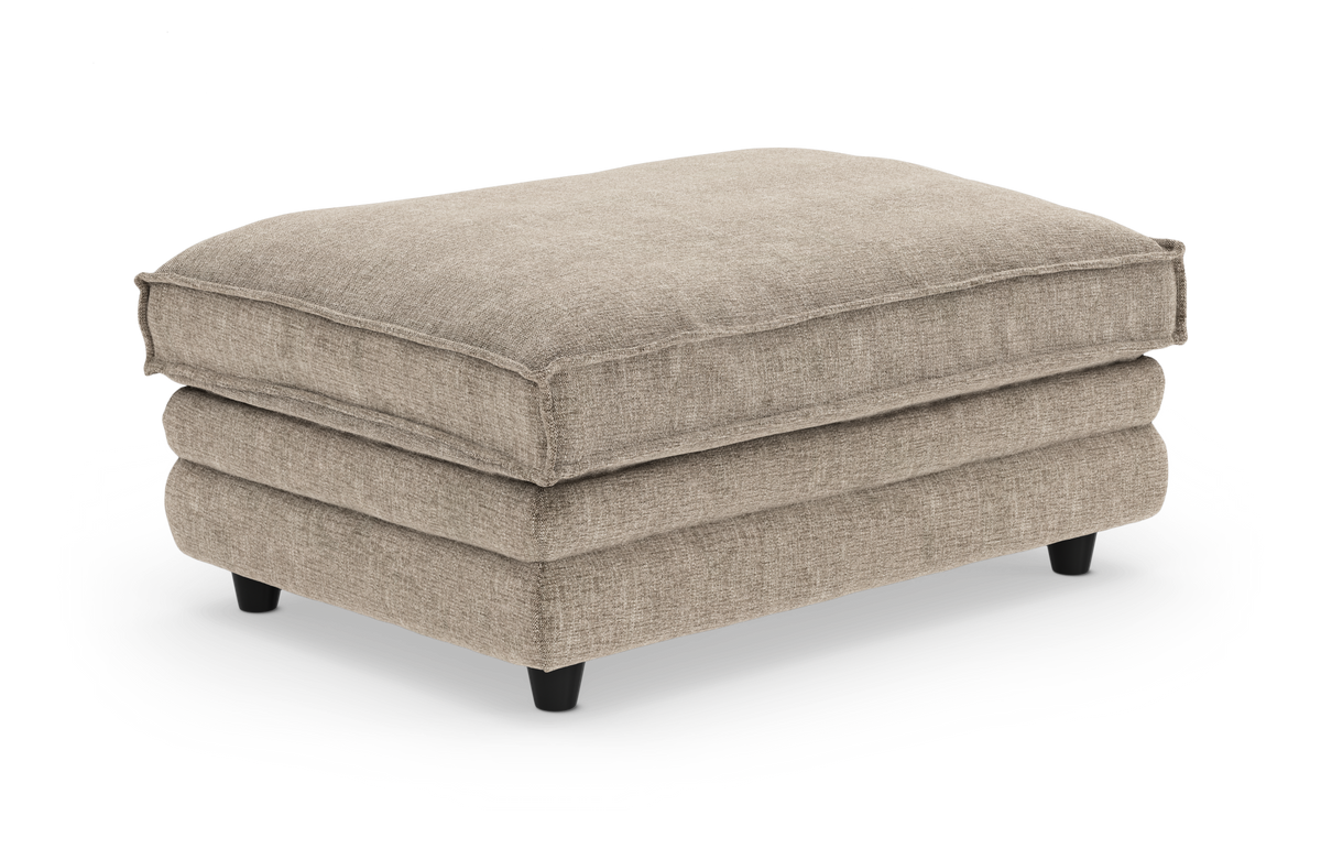 Beige stofpuf med bløde, stablede puder og korte sorte ben, frilagt på hvid baggrund.