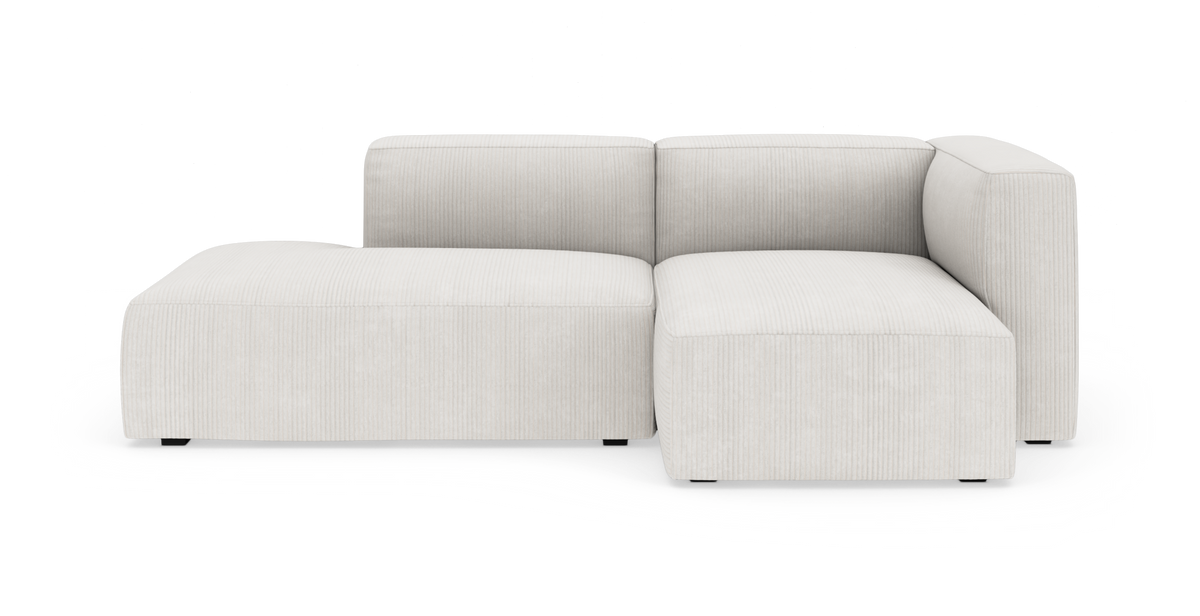 Lys beige modulsofa med venstre chaiselong og højrearmet hjørnemodul i rillet stof, frilagt på hvid baggrund.