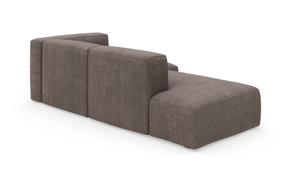 Modulsofa i brungrå bredriflet fløjl, lav profil med chaiselong på højre side, frilagt på hvid baggrund i bagfra skrå vinkel.
