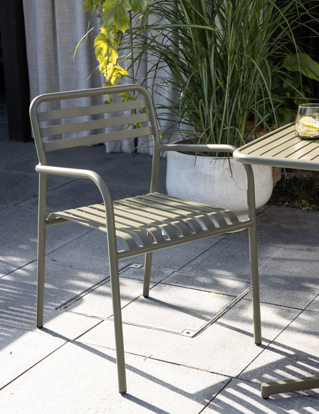 Olivengrøn udestol i metal med lameller ved siden af matchende bord på terrasse med potteplanter og et glas med citron.