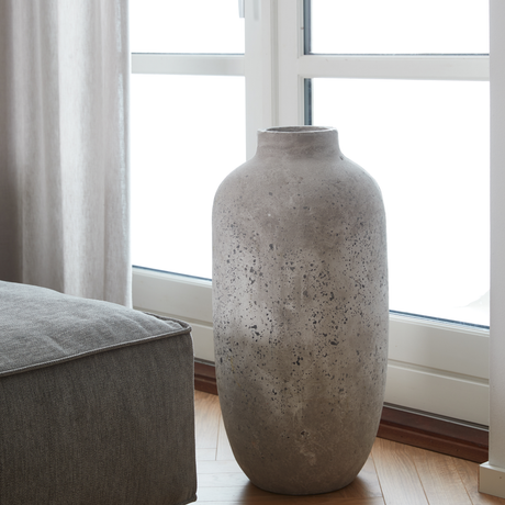 Stor grå betonvase ved et vindue i en lys stue.