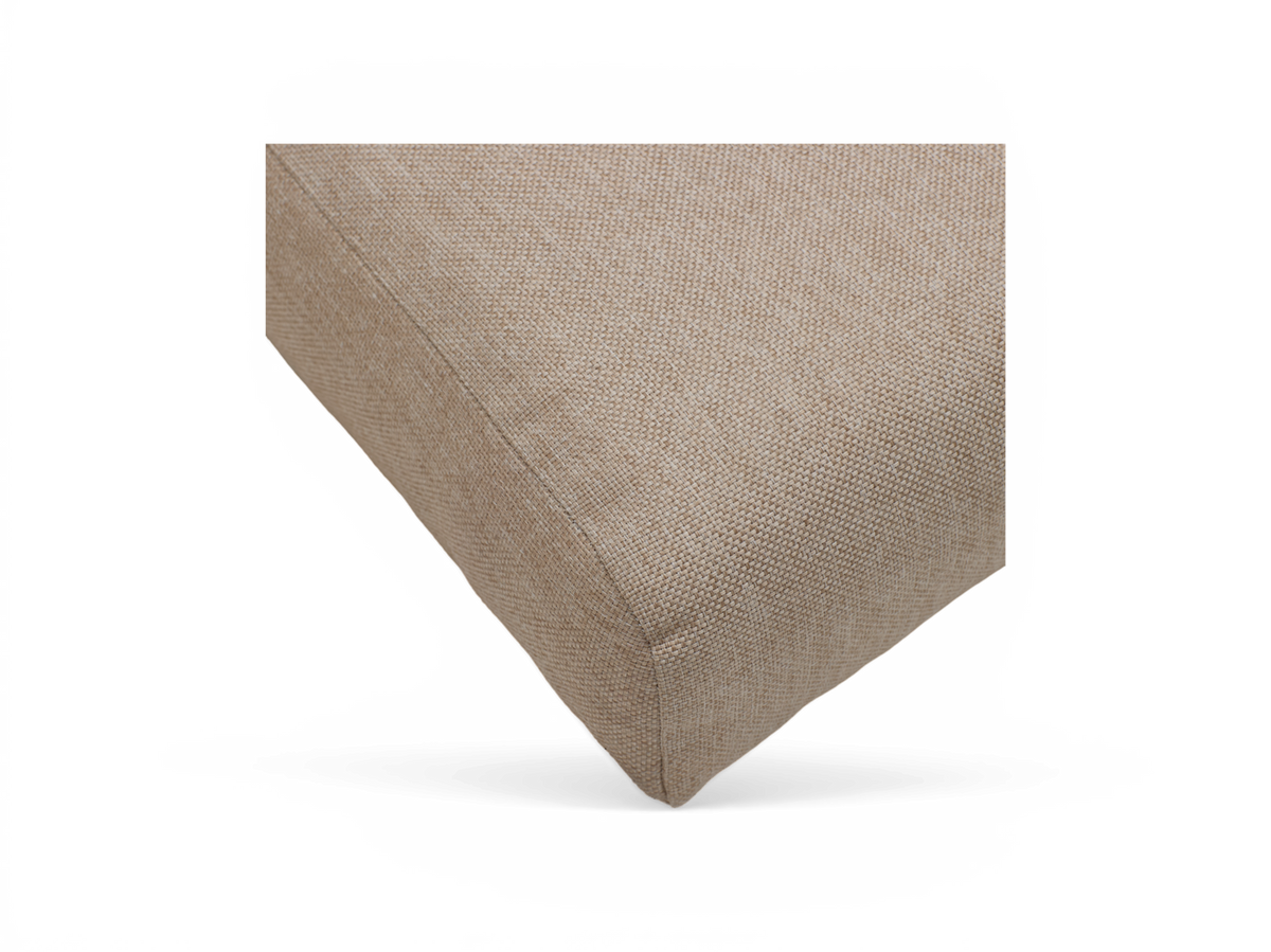 Beige pude i groft vævet stof, nærbillede af et hjørne på hvid baggrund.