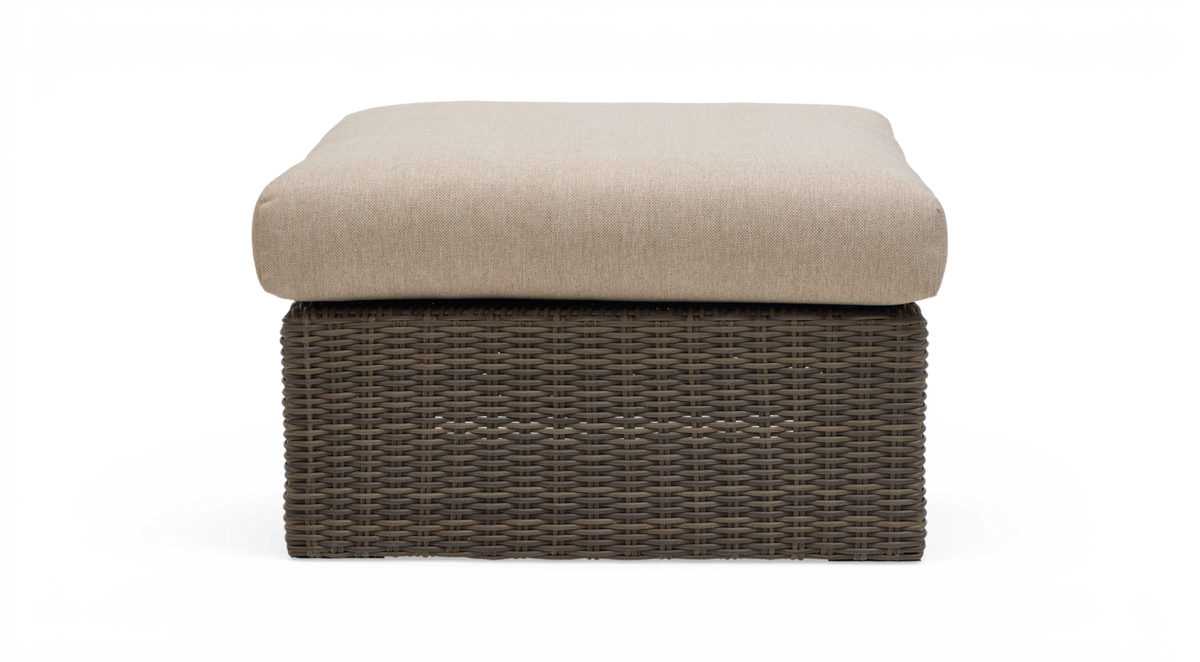Frontvisning af en kvadratisk ottoman med beige hynde og brun flettet rattanbase på hvid baggrund.