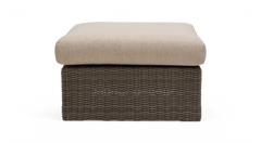 Frontvisning af en kvadratisk ottoman med beige hynde og brun flettet rattanbase på hvid baggrund.