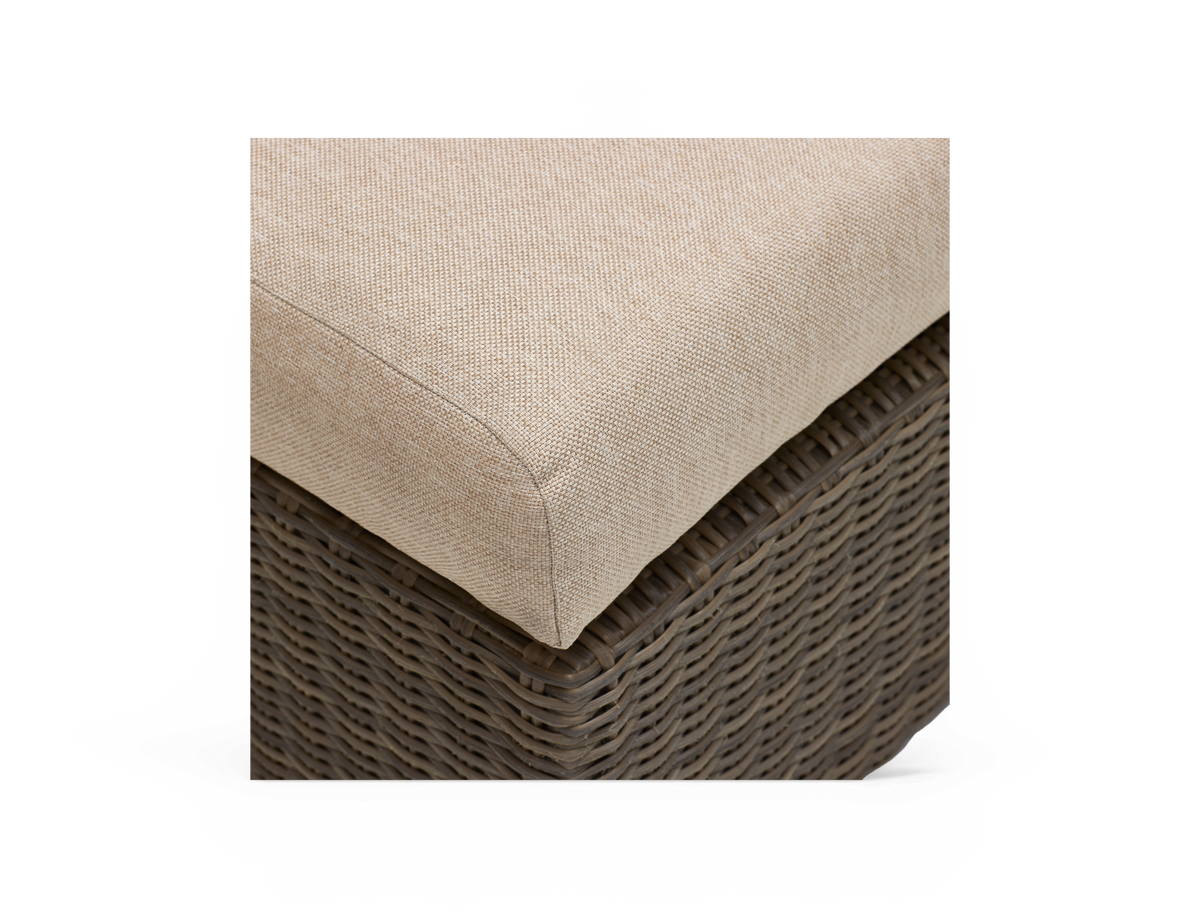 Nærbillede af beige hynde på brun flet-/rottingmøbel, produktdetalje mod hvid baggrund.