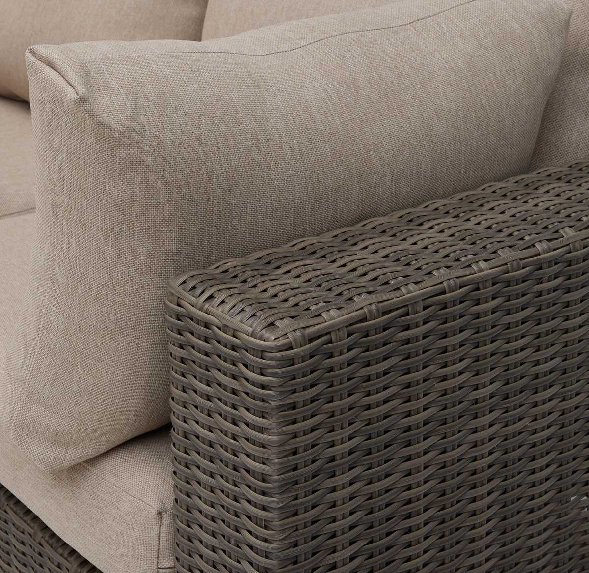 Nærbillede af beige sofa med pude og brunflettet rattan-armlæn.