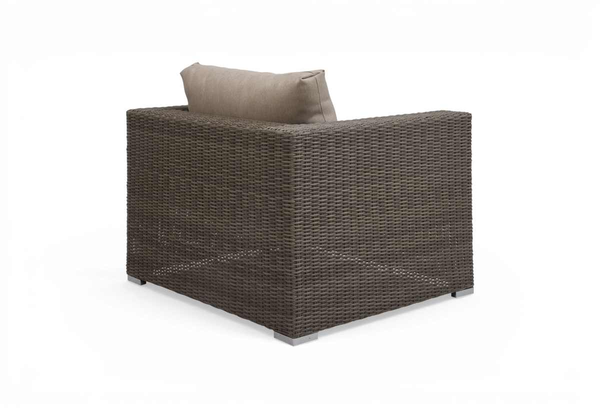Brun rattan lænestol med beige rygpude, fotograferet bagfra i vinkel på hvid baggrund.