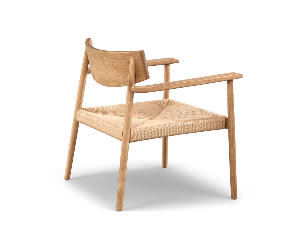 Minimalistisk armstol i lyst træ med flettet sæde, set skråt bagfra på hvid baggrund.