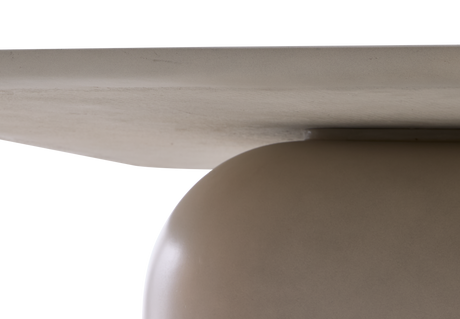 Nærbillede af en minimalistisk borddetalje: lys, flad bordplade møder en rund beige søjlebase i studielys.