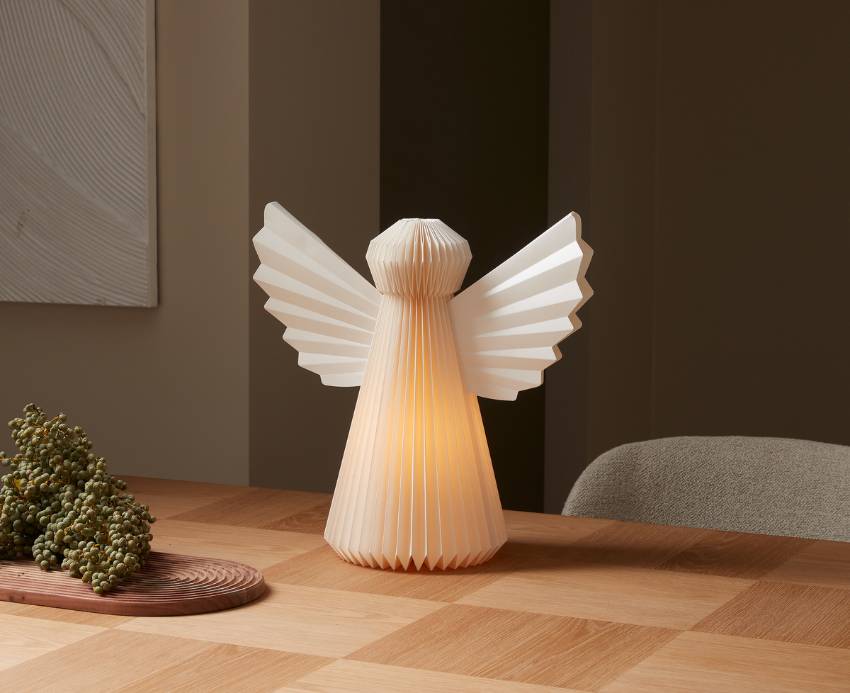 Foldet papirengel som bordlampe lyser varmt på et træbord i et minimalistisk interiør.