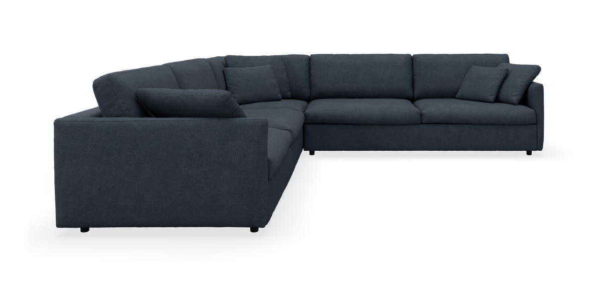 Mørkeblå L-formet hjørnesofa med løse puder, frilagt mod sort baggrund.